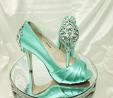 A pair of high heeled aqua blue satin shoes with a peep toe and a hidden platform at the front of the shoes and a crystal design on the front of the shoes and a crystal design on the back heel of the shoes