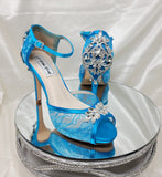 A pair of turquoise high heeled platform lace shoes with an ankle strap and a crystal design on the front of the peep toe shoes and a crystal design on the back heel of the shoes