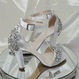 A pair of white high block heel shoes with an ankle strap and a crystal and pearl design on the front toe strap of the shoes and a large crystal design on the back heel of the shoes