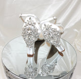 A pair of white block heel shoes with an ankle strap and a crystal design on the front toe strap and a crystal design on the back heel of the shoes