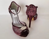 A pair of burgundy high heeled platform lace shoes with an ankle strap and a crystal design on the front of the peep toe shoes