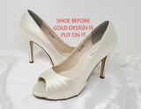 A pair of high heeled ivory satin shoes with a peep toe and a hidden platform at the front of the shoes and a gold crystal design on the back heel of the shoes