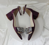 a pair of eggplant purple block heel bridal shoes with an ankle strap and a pearl and crystal design on the front strap of the shoes