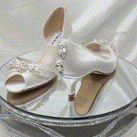 A pair of  bridal shoes in ivory satin with a kitten heel and a peep toe and a pearl and crystal design on the front and back heel of the shoes