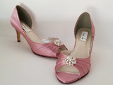 A pair of dusty rose satin medium height heel shoes with a peep toe and designed with a crystal design on the front of the shoes 
