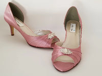 A pair of dusty rose satin medium height heel shoes with a peep toe and designed with a crystal design on the front of the shoes