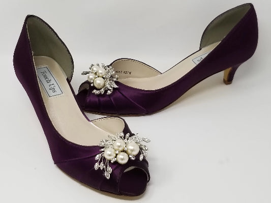 A pair of eggplant purple satin kitten heels with a peep toe and designed with a crystal design on the front of the shoes