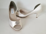 A pair of ivory satin medium height heel shoes with a peep toe and designed with a crystal design on the front of the shoes