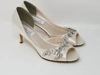 A pair of ivory satin medium height heel shoes with a peep toe and designed with a crystal vine design on the front and side of the shoes