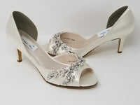 A pair of ivory satin medium height heel shoes with a peep toe and designed with a crystal vine design on the front and side of the shoes