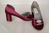 A pair of burgundy shoes with a low block heel and a peep toe front with a crystal design on the front of the shoes