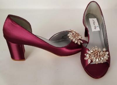 A pair of burgundy shoes with a low block heel and a peep toe front with a rose gold crystal design on the front of the shoes