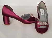 A pair of burgundy shoes with a low block heel and a peep toe front with a rose gold crystal design on the front of the shoes