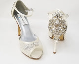 A pair of ivory high heeled platform lace shoes with an ankle strap and a crystal design on the front of the peep toe shoe and a crystal design on the back heel of the shoes