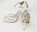 A pair of ivory high heeled platform lace shoes with an ankle strap and a crystal design on the front of the peep toe shoe and a crystal design on the back heel of the shoes