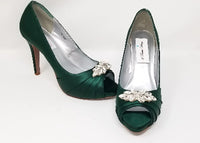 A pair of high heeled hunter green satin shoes with a peep toe and a hidden platform at the front of the shoes and a crystal design on the front of the shoes