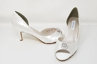 A pair of white satin medium height heel shoes with a peep toe and designed with a crystal design on the front of the shoes