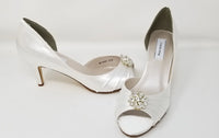A pair of white satin bridal shoes with a peep toe and designed with a crystal design on the front of the shoes