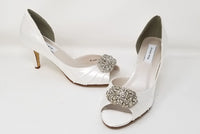 A pair of white satin bridal shoes with a peep toe and designed with a crystal design on the front of the shoes