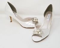 A pair of ivory satin wedding heels with a peep toe and designed with a crystal and pearl design on the front of the shoes 