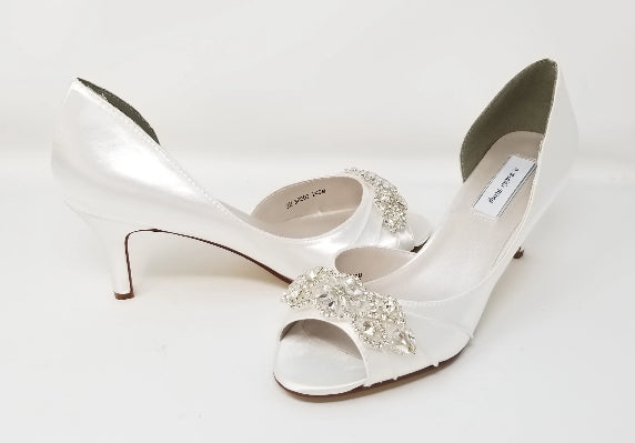 A pair of white satin bridal shoes with a peep toe and designed with a crystal design on the front of the shoes
