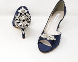 A pair of navy blue satin medium height heel shoes with a peep toe and designed with a crystal design on the front of the shoes and a crystal design on the back heel of the shoes