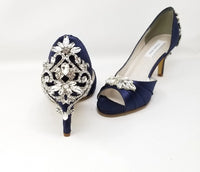 A pair of navy blue satin medium height heel shoes with a peep toe and designed with a crystal design on the front of the shoes and a crystal design on the back heel of the shoes