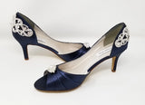 A pair of navy blue satin medium height heel shoes with a peep toe and designed with a crystal design on the front of the shoes shoes and a crystal design on the back heel of the shoes