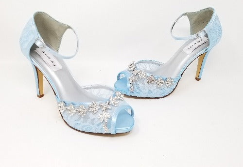 A pair of baby blue high heeled platform lace shoes with an ankle strap and a crystal design on the front and side of the peep toe shoe
