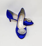 A pair of royal blue satin kitten heel shoes with a peep toe and a crystal design on the front of the shoes