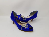 A pair of royal blue satin kitten heel shoes with a peep toe and a crystal and pearl design on the side of the shoes