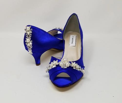 A pair of royal blue satin kitten heel shoes with a peep toe and a crystal and pearl design on the front and the back heel of the shoes