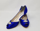 A pair of royal blue satin kitten heel shoes with a peep toe with a small crystal design on the front of the shoes
