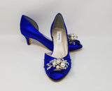 A pair of royal blue satin kitten heel shoes with a peep toe and a crystal and pearl design on the front of the shoes