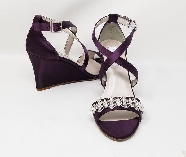 A pair of eggplant purple wedding shoes with high wedge and straps across the front of the foot designed with a crystal design on the front toe strap of the shoes 