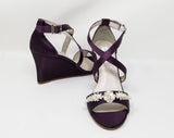 A pair of eggplant purple wedding shoes with high wedge and straps across the front of the foot designed with a pearl and crystal design on the front toe strap of the shoes 