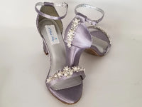 A pair of lilac purple block heel shoes with an ankle strap and a crystal and pearl design on the front toe strap of the shoes and a crystal and pearl design on the heel of the shoes