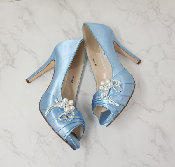 A pair of high heeled baby blue satin shoes with a peep toe and a hidden platform at the front of the shoes and a pearl and crystal design on the front of the shoes