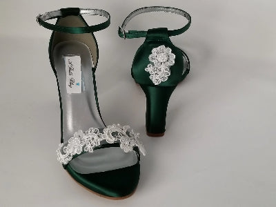A pair of hunter green block heel shoes with an ankle strap and a lace and pearl design on the front toe strap of the shoes and a lace and pearl design on the heel of the shoes