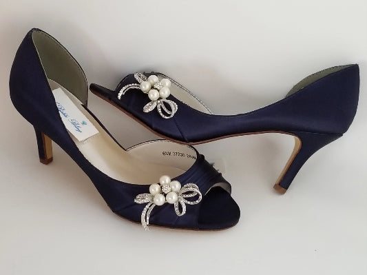 A pair of navy blue satin medium height heel shoes with a peep toe and designed with a pearl and crystal design on the side of the shoes
