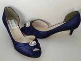 A pair of navy blue satin kitten heel shoes with a peep toe with a small crystal design on the front of the shoes