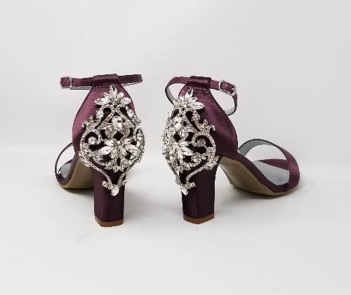 A pair of eggplant purple block heel shoes with an ankle strap and a crystal design on the front toe strap of the shoes and a crystal design on the heel of the shoes