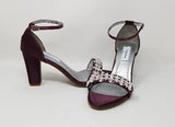 A pair of eggplant purple block heel shoes with an ankle strap and a crystal design on the front toe strap of the shoes