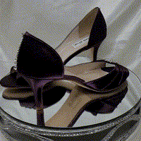 A pair of eggplant purple satin medium height heel bridal shoes with a peep toe and designed with a crystal design on the front of the shoes and a crystal teardrop design on the back heel of the shoes