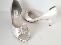 a pair of white medium height heels with a peep toe and a large crystal design on the front of the shoes