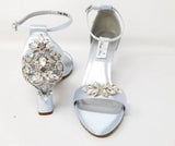 A pair of baby blue block heel shoes with an ankle strap and a crystal design on the front toe strap of the shoes and a crystal design on the heel of the shoes