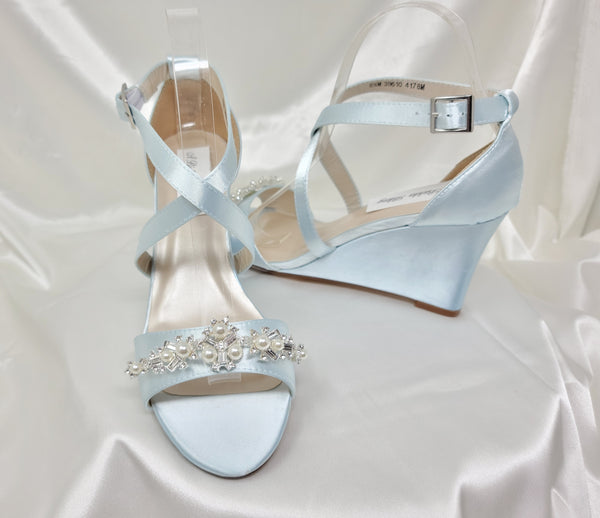 A pair of baby blue wedding shoes with high wedge and straps across the front of the foot designed with a pearl and crystal design on the front toe strap of the shoes