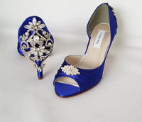 A pair of royal blue satin medium height heel bridal shoes with a peep toe and designed with a crystal design on the front of the shoes and a crystal design on the back heel of the shoes