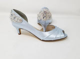 A pair of baby blue satin kitten heels with a peep toe and designed with a crystal design on the front of the shoes and a large crystal design on the back heel of the shoes