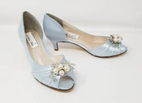 A pair of baby blue satin kitten heels with a peep toe and designed with a pearl and crystal design on the front of the shoes